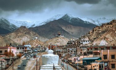 Panoramic view of Leh town with Himalayan mountains and traditional architecture under a dramatic sky.