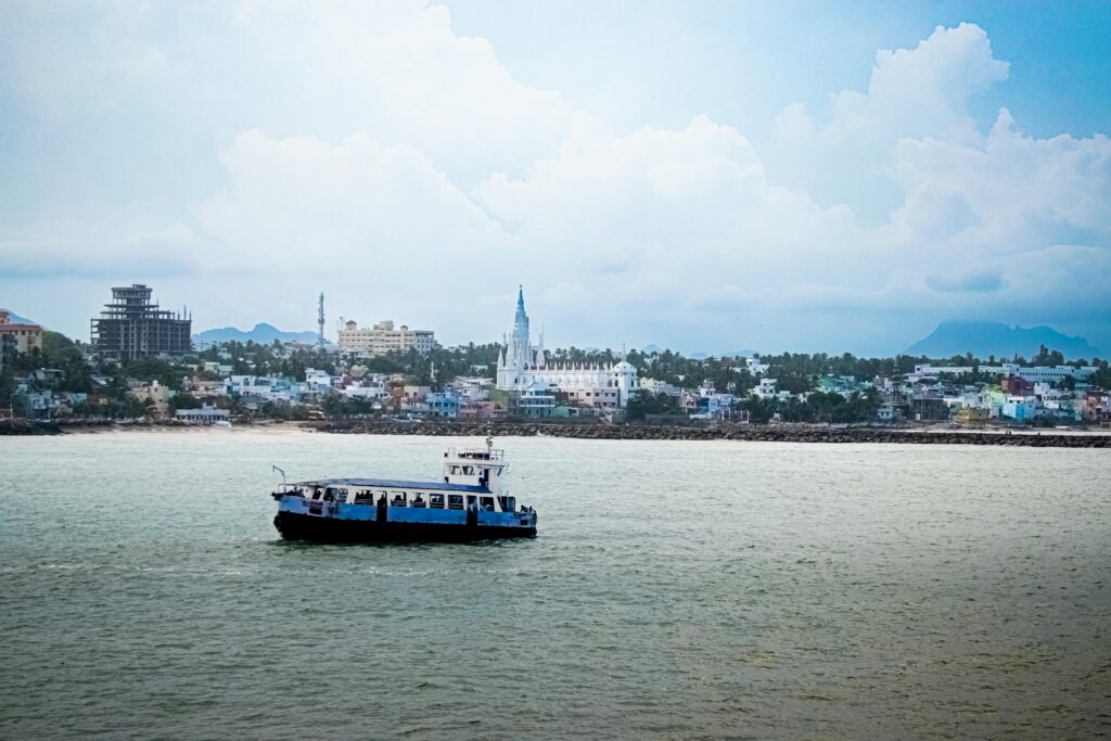 A passenger ship sails past the scenic waterfront of Kanyakumari, India, with urban landscapes in the background.