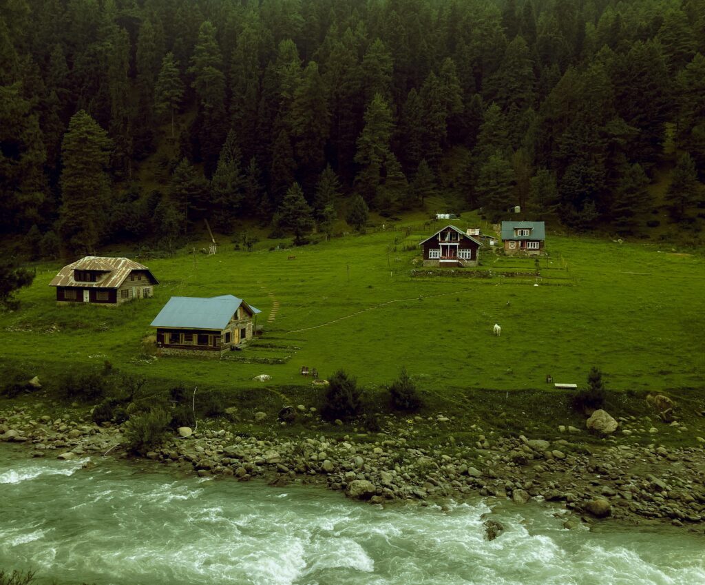 Charming cottages by a river in Pahalgam surrounded by lush green forests.