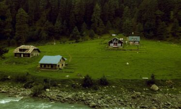 Charming cottages by a river in Pahalgam surrounded by lush green forests.