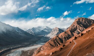 Breathtaking aerial view of Spiti Valley's snow-capped mountains and winding roads under a vibrant blue sky.
