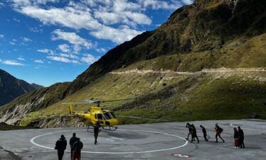 A scenic view of people near a helicopter on a mountain helipad under a blue sky.