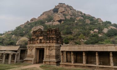 Explore the ancient stone temple ruins at Hampi, showcasing historic architecture against rocky hills.