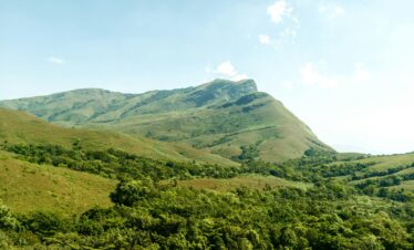 Lush green mountain range in Kudremukh, India under a clear summer sky.