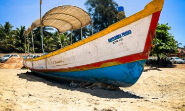 A vibrant fishing boat sits on the sandy beach under a bright blue sky in Gokarna, India.