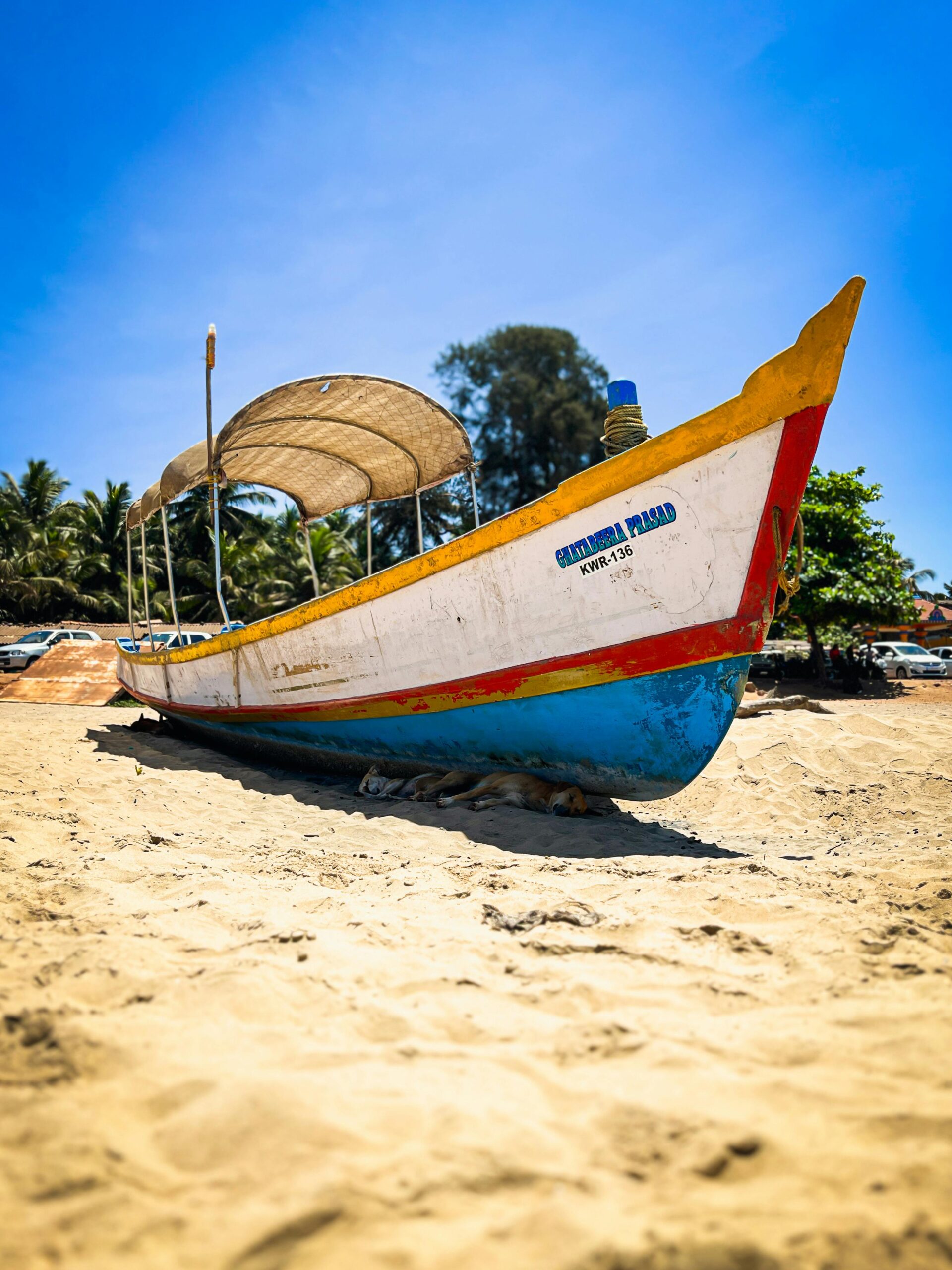 A vibrant fishing boat sits on the sandy beach under a bright blue sky in Gokarna, India.