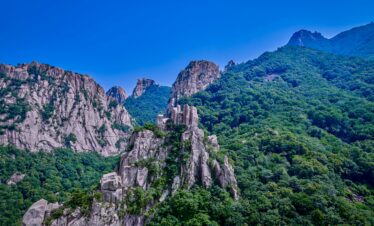 Beautiful landscape of rugged mountains and lush green forests under a clear blue sky.