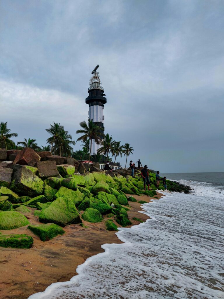 A stunning view of a lighthouse on the Indian coast, surrounded by palm trees and mossy rocks.