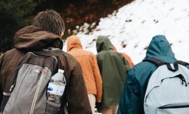 A group of hikers with backpacks walking on a snowy mountain trail in winter.
