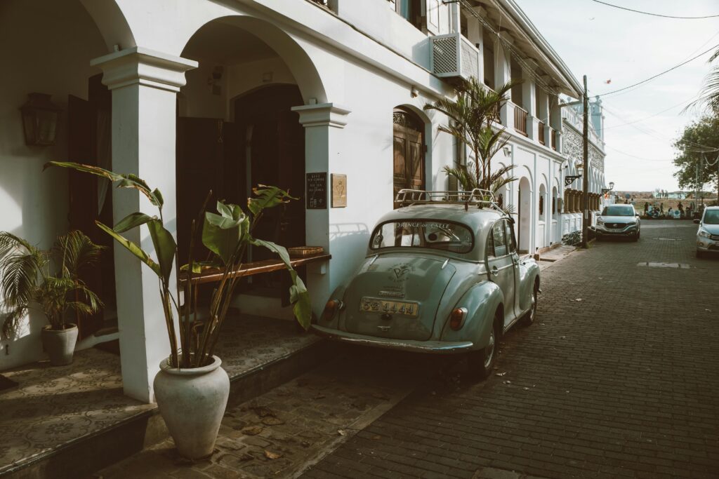 Vintage car parked on a charming street with colonial architecture and lush greenery.