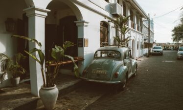 Vintage car parked on a charming street with colonial architecture and lush greenery.