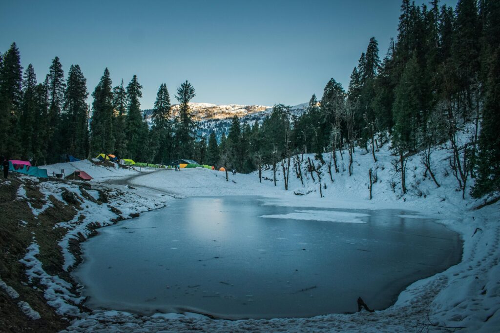 A stunning winter scene of a frozen lake surrounded by snow-covered trees in Uttarakhand, India.
