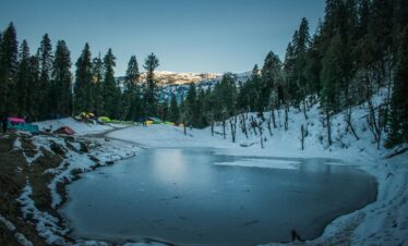 A stunning winter scene of a frozen lake surrounded by snow-covered trees in Uttarakhand, India.